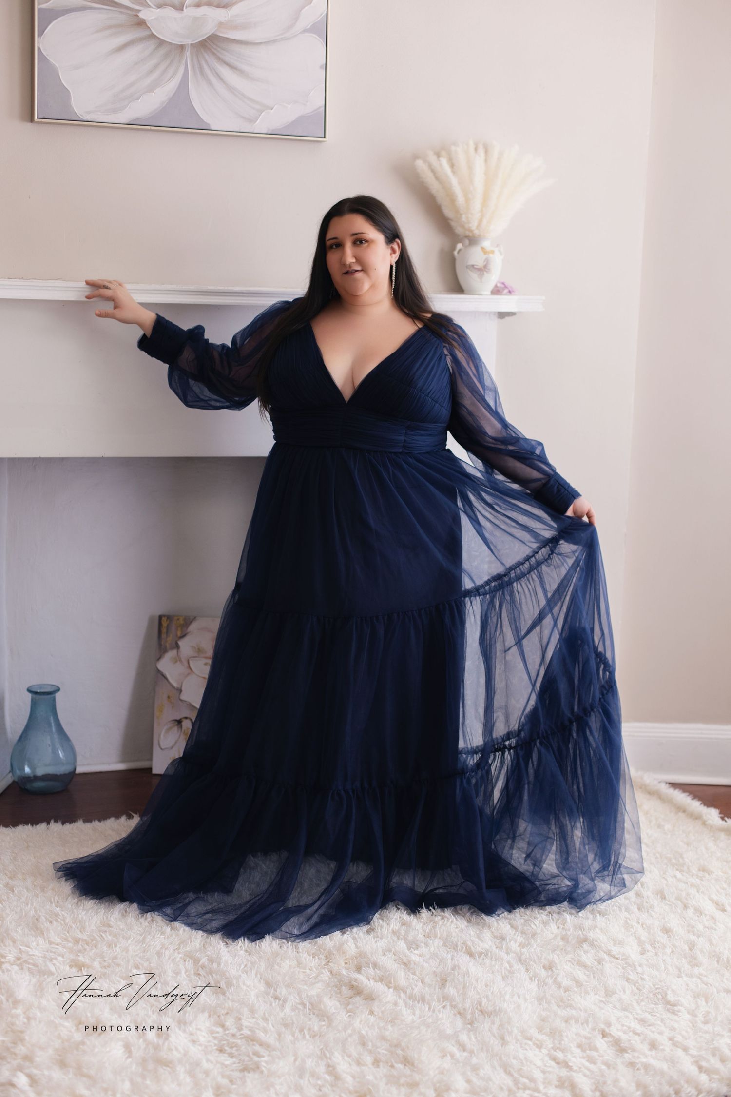 Dramatic pose in navy blue tulle gown against white interior setting.