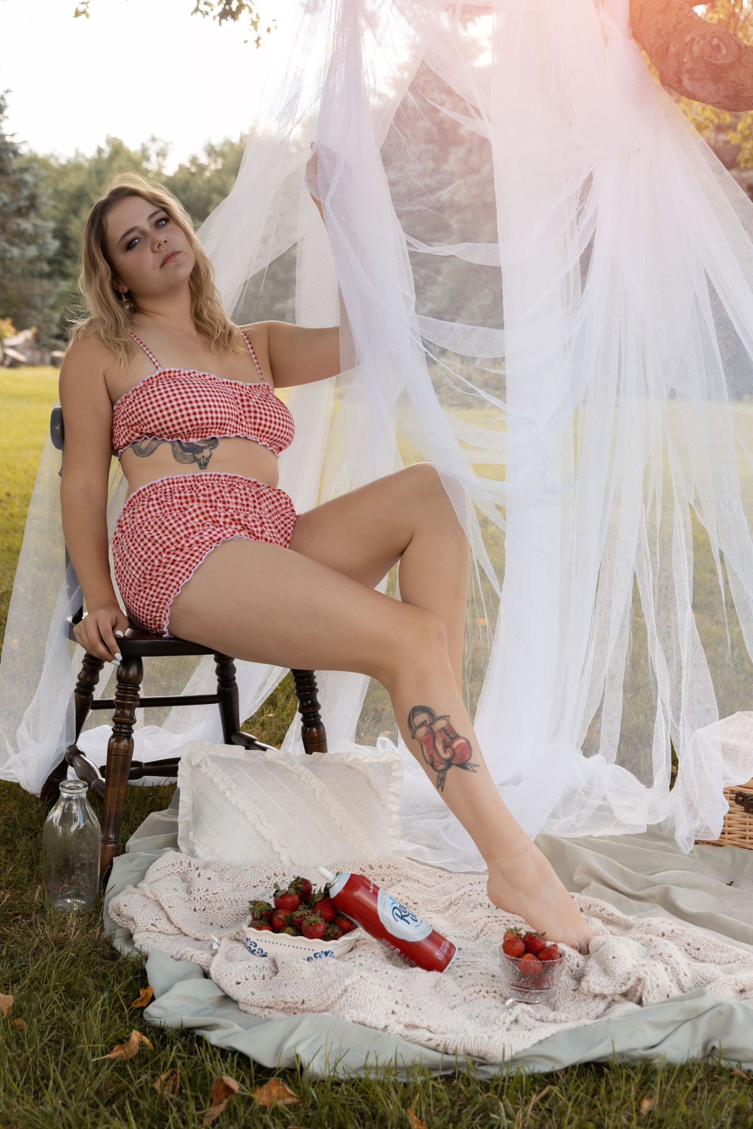 Woman in red gingham two-piece outfit posing at outdoor picnic setup with sheer canopy.