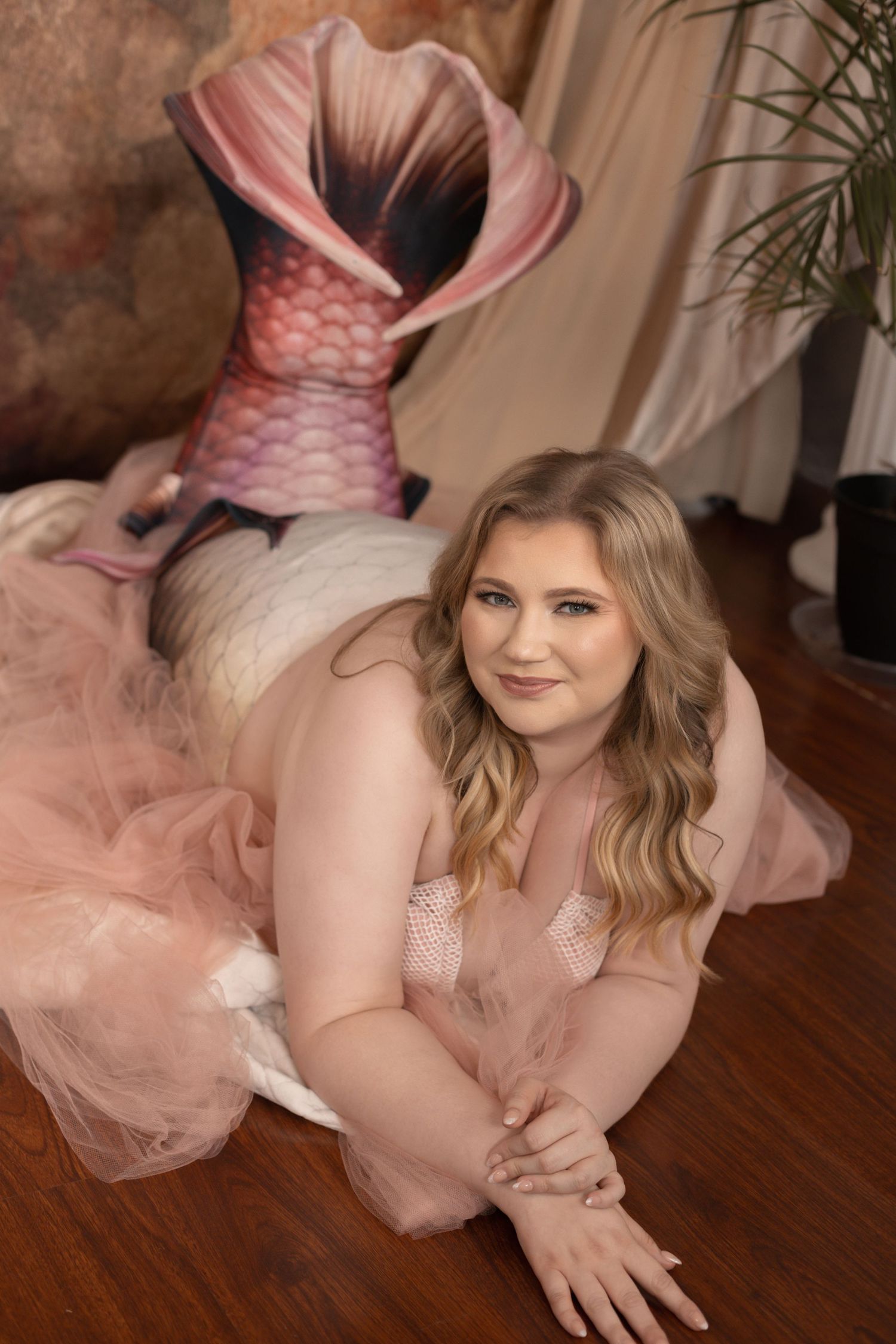 Woman in pink tulle skirt and mermaid costume poses on wooden floor in a studio setting.