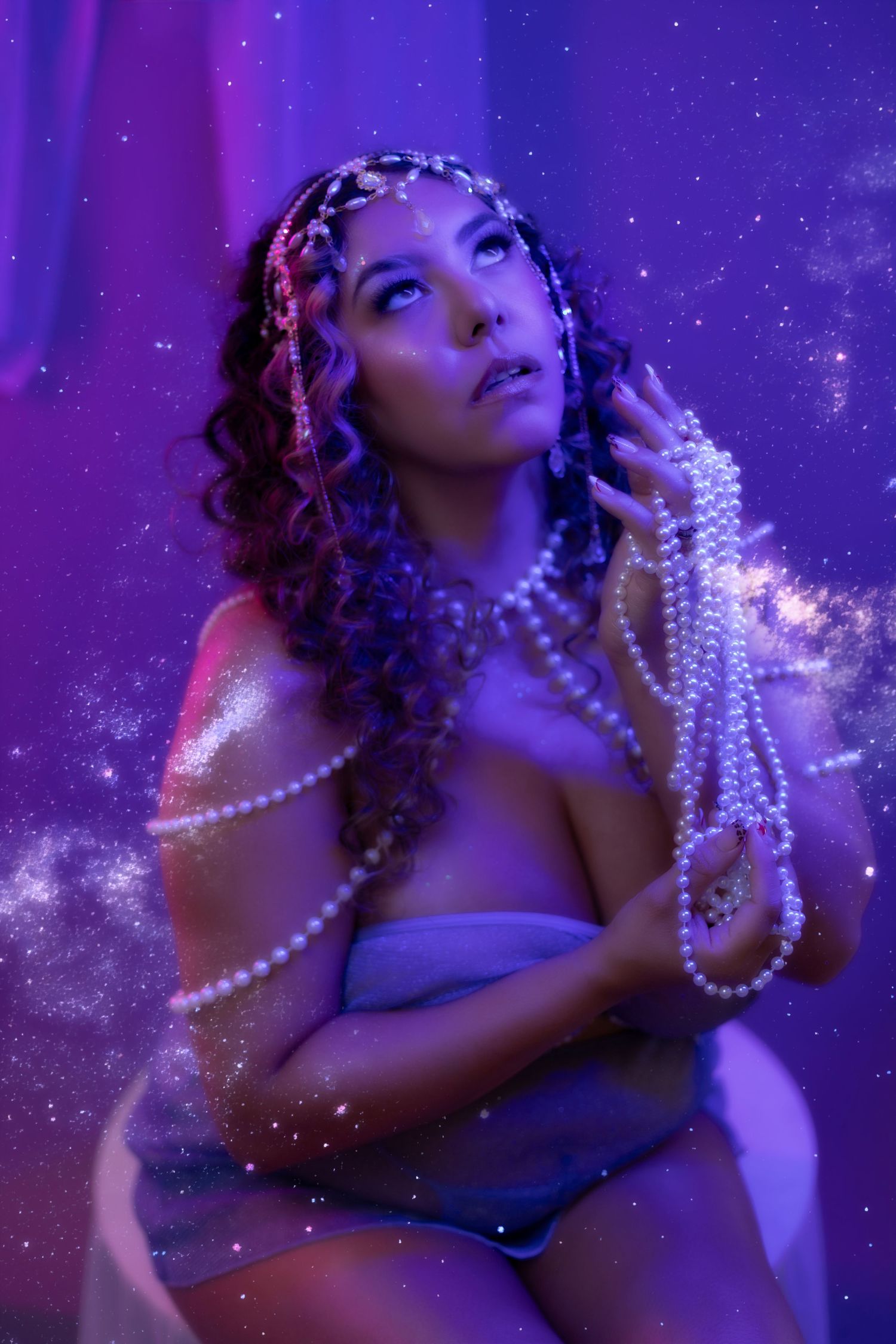 Woman adorned with pearl jewelry and floral headpiece poses in dreamy purple neon light with cosmic sparkles.
