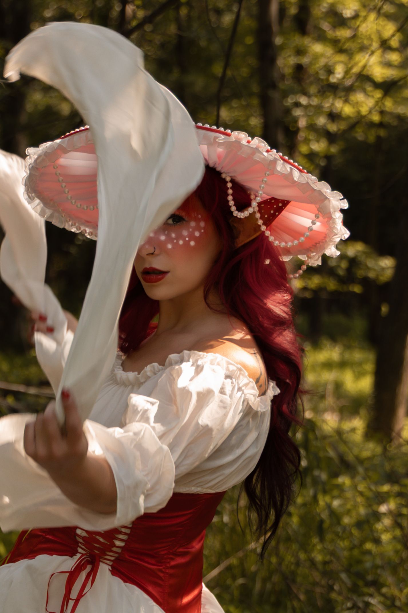 Woman in red corset, white off-shoulder blouse, and decorative mushroom hat with face paint poses in forest.