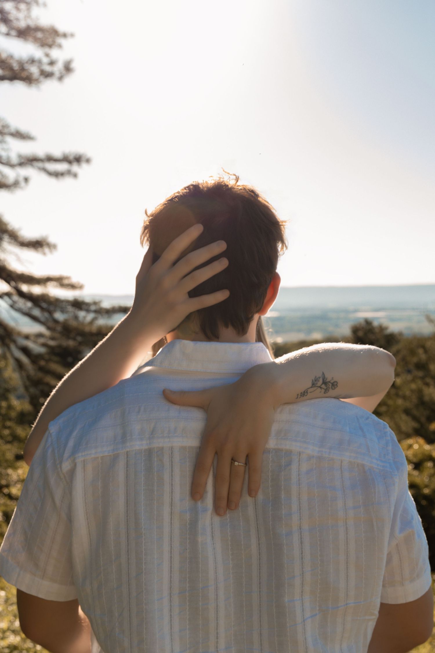 Person in white linen shirt viewed from behind with hand on head, overlooking scenic ocean horizon on sunny day.