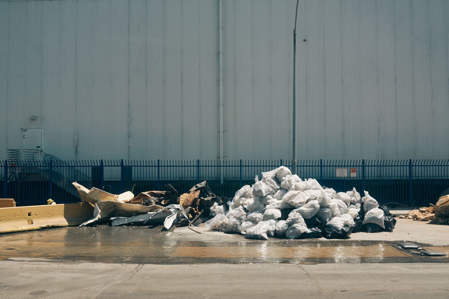 Pile of white bags and debris dumped outside an industrial building on a concrete surface.
