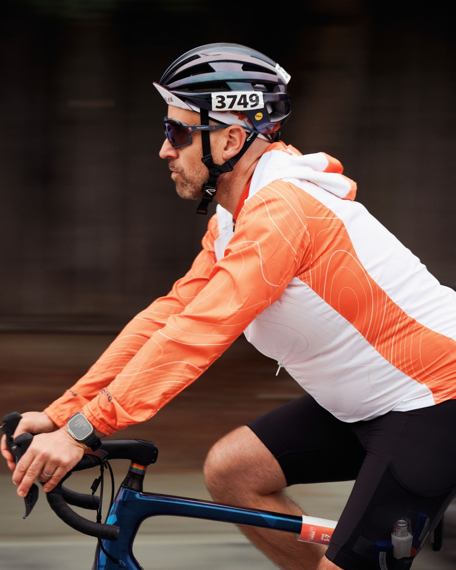 Cyclist wearing orange and white cycling gear with helmet and sunglasses rides a road bike.