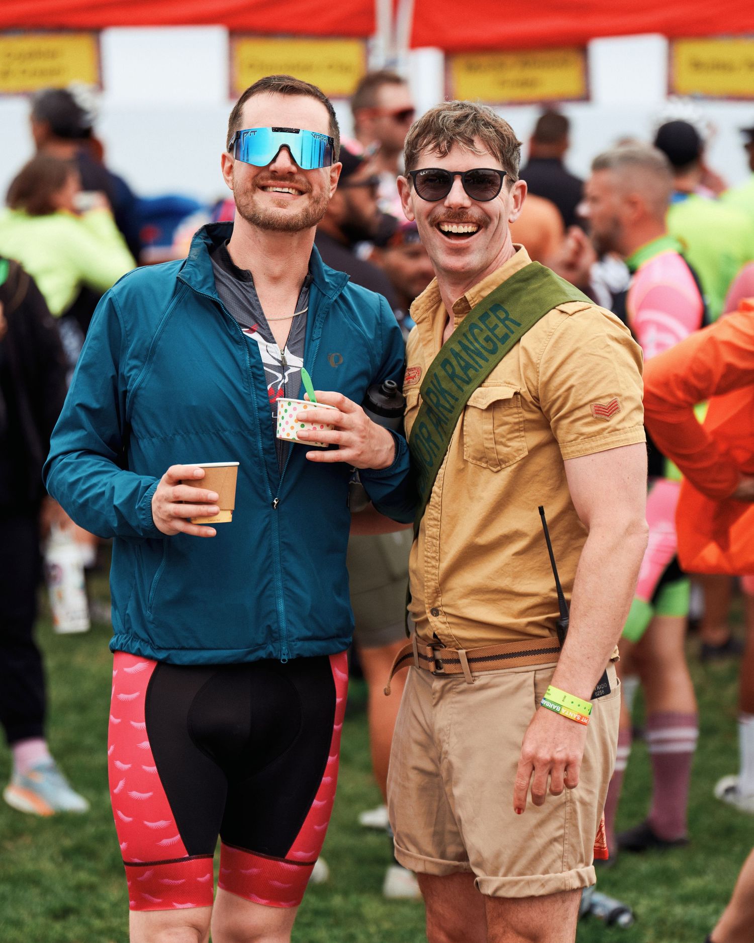Two friends in athletic wear and sunglasses enjoying beverages at outdoor festival.