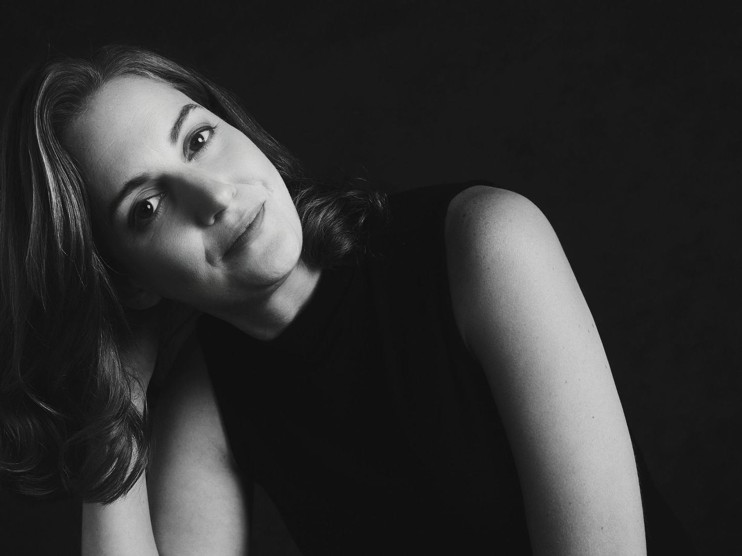 Black and white portrait of a young woman in a sleeveless top, gazing thoughtfully against a dark background.