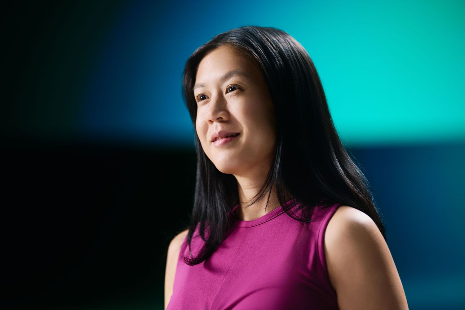 Portrait of someone in a magenta sleeveless top looking upward with a thoughtful expression against a teal backdrop.