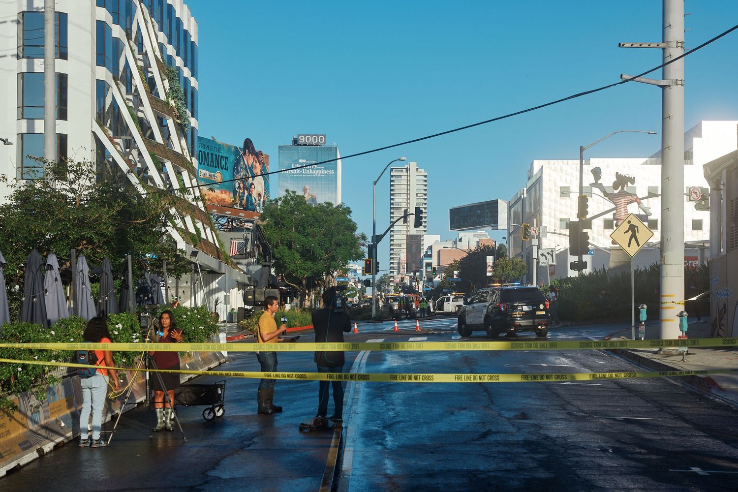 News crews report from behind fire-line tape as sheriff's deputies and utility crews hold a closure on Holloway Drive near Sunset Boulevard.