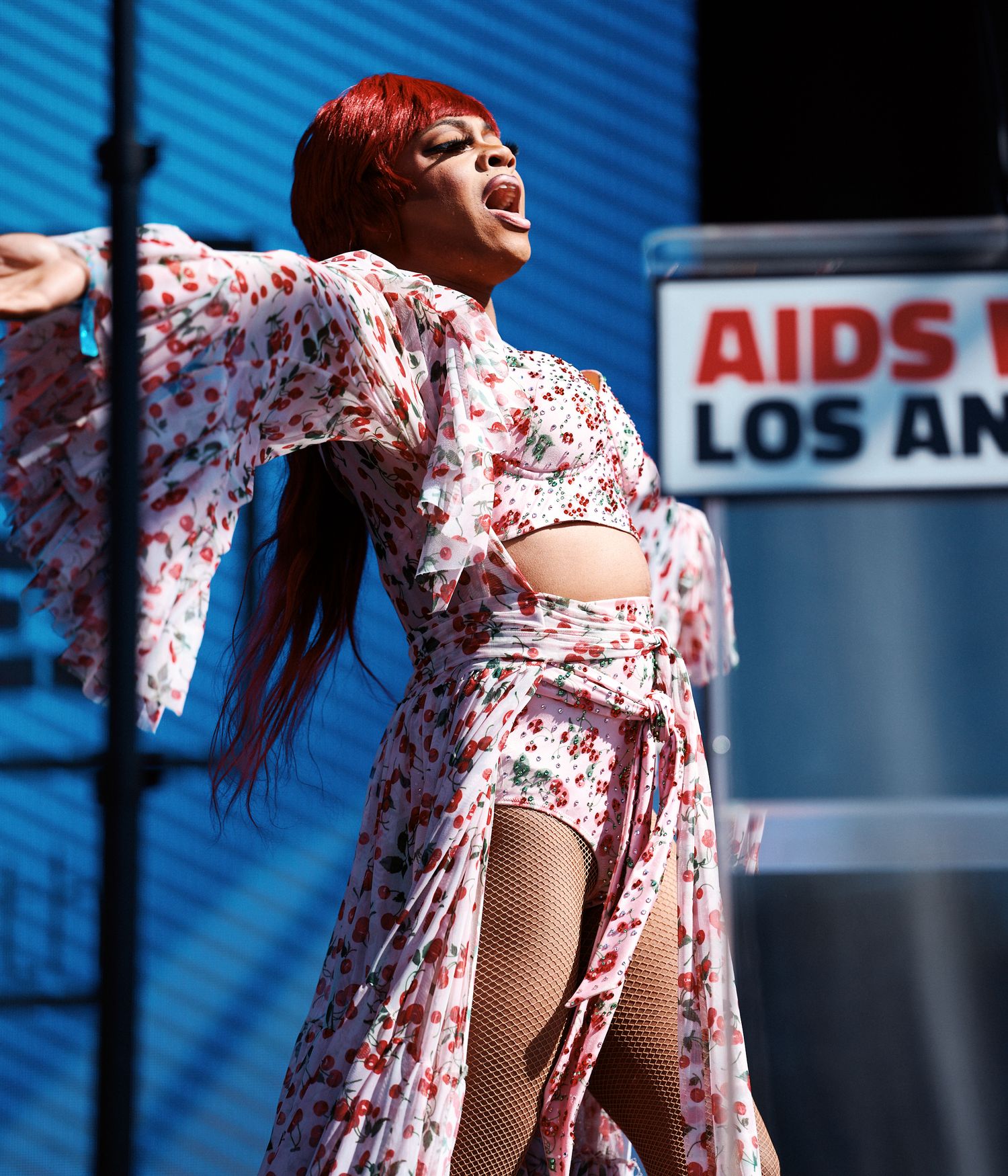 A person in a floral print dress dances and twirls against a blue background with urban signage visible.