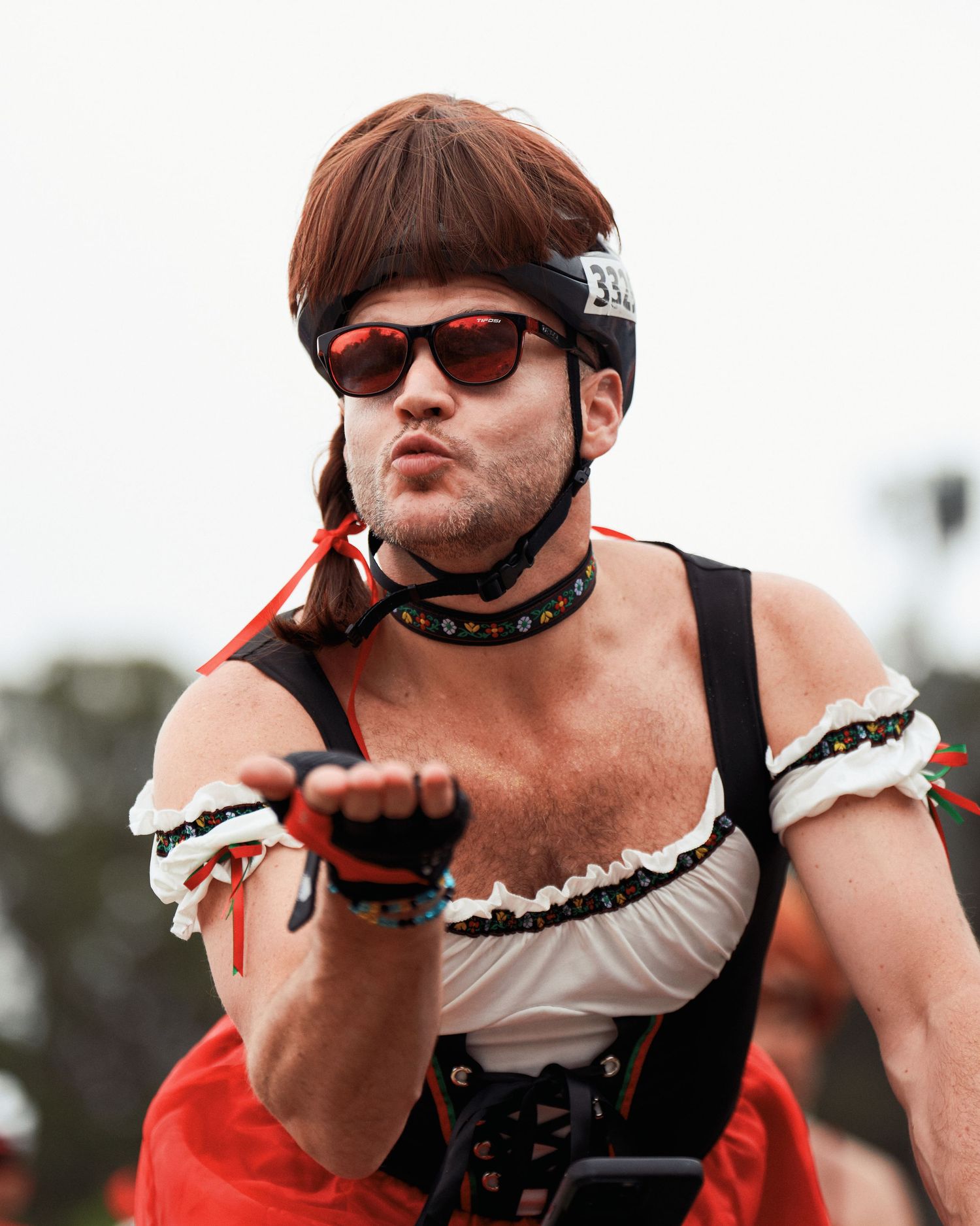 Person wearing sunglasses, a choker, and white ruffled outfit poses dramatically against an overcast sky.
