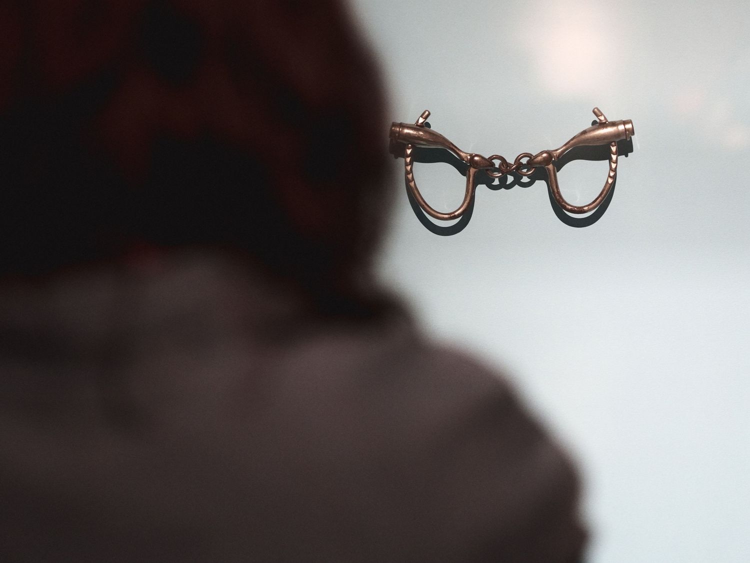 Antique copper handcuffs in a glass case, seen past a blurred visitor, at the Autry’s “Life, Liberty, and Los Angeles.”