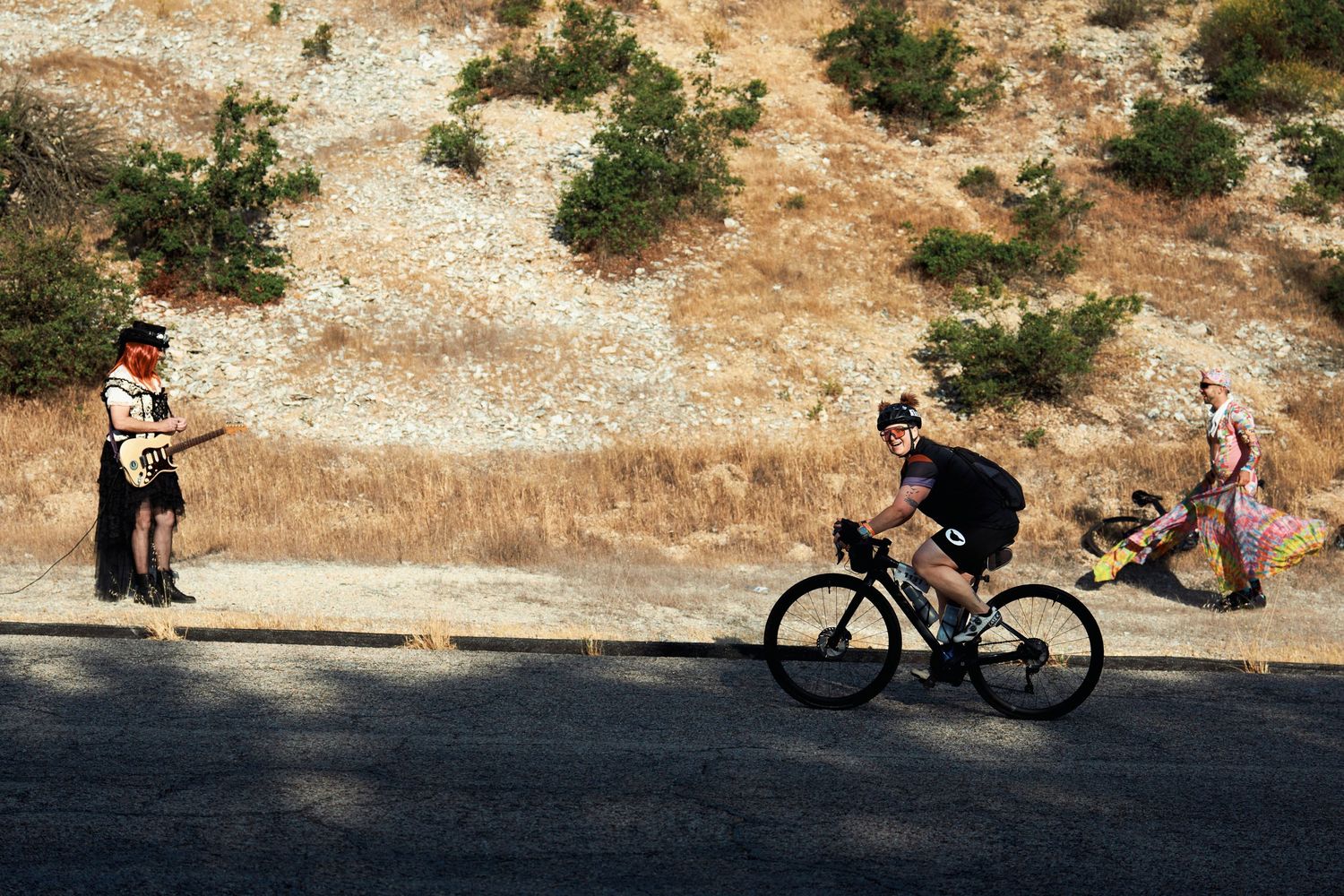 A cyclist rides on a winding mountain road while onlookers stand by during a race or cycling event.