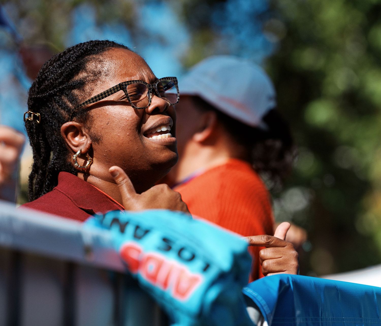 A person wearing glasses and braided hair speaks passionately into a microphone at an outdoor event.