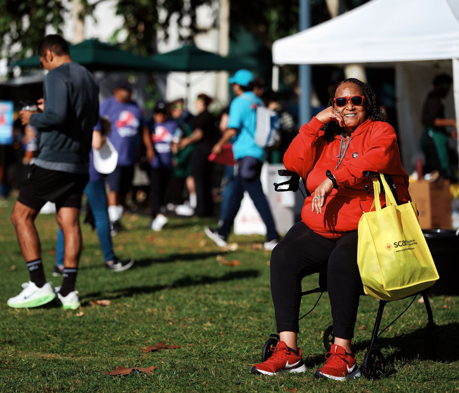A close-up view of red sneakers and a bright yellow shopping bag on grass during an outdoor gathering.