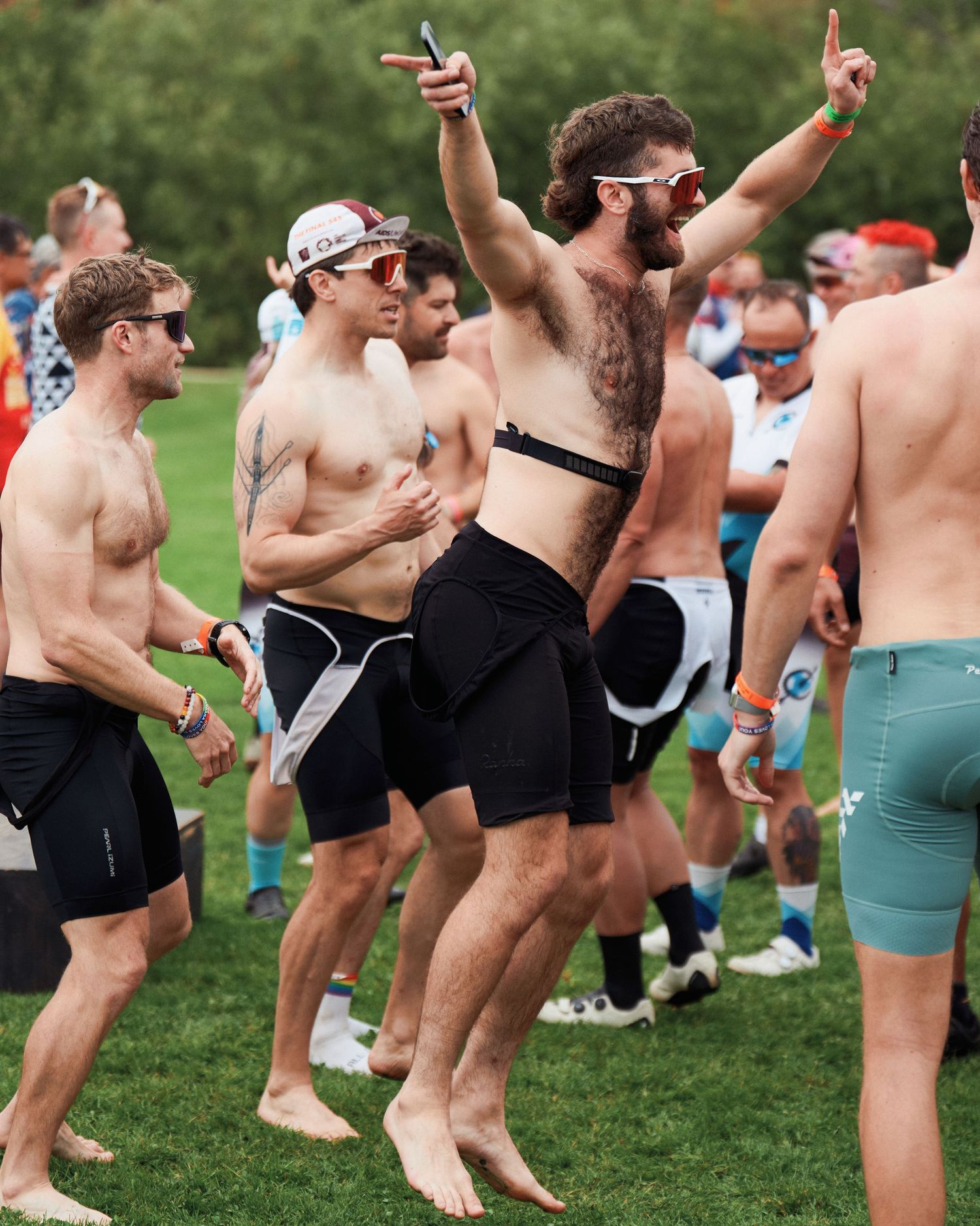 Shirtless crowd enjoying an outdoor summer event with people dancing and celebrating on grass field.