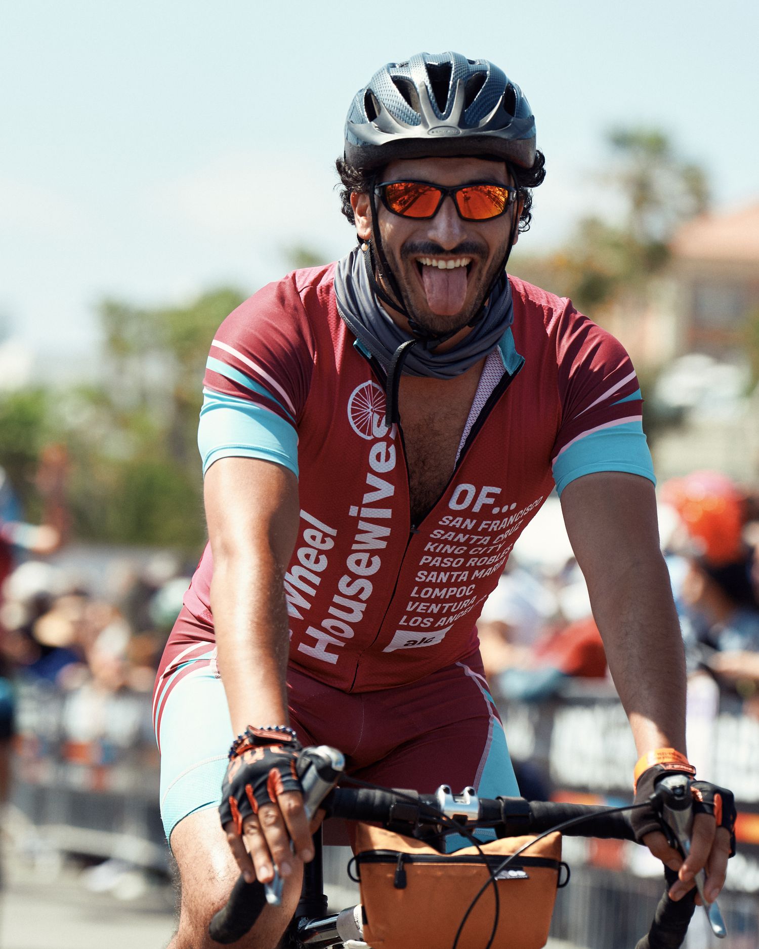 Cyclist wearing red jersey and helmet smiles while riding bike in sunny outdoor event.
