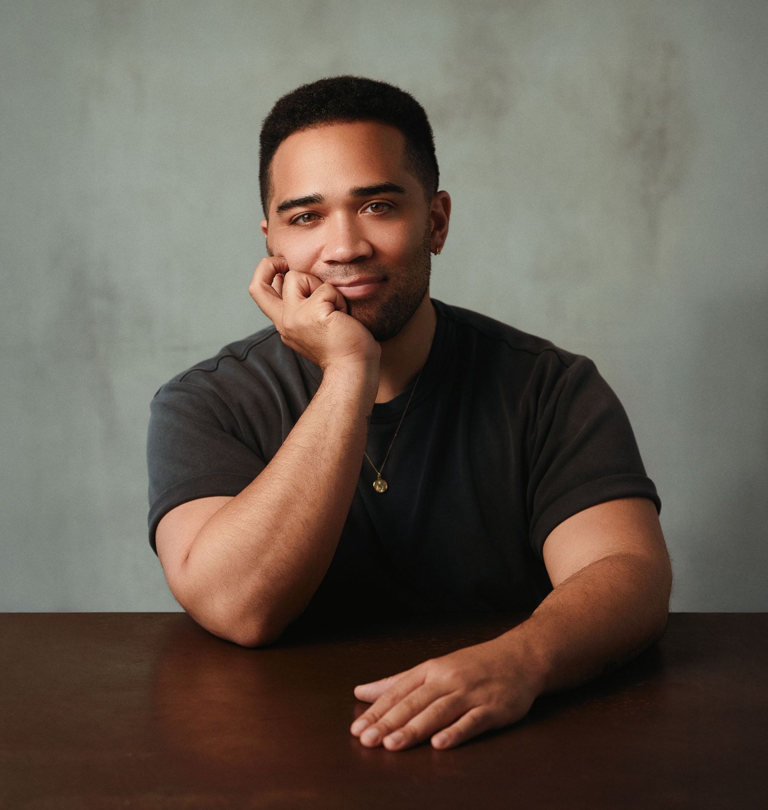 Person in black t-shirt rests head on hand while posing against textured gray background in portrait series.