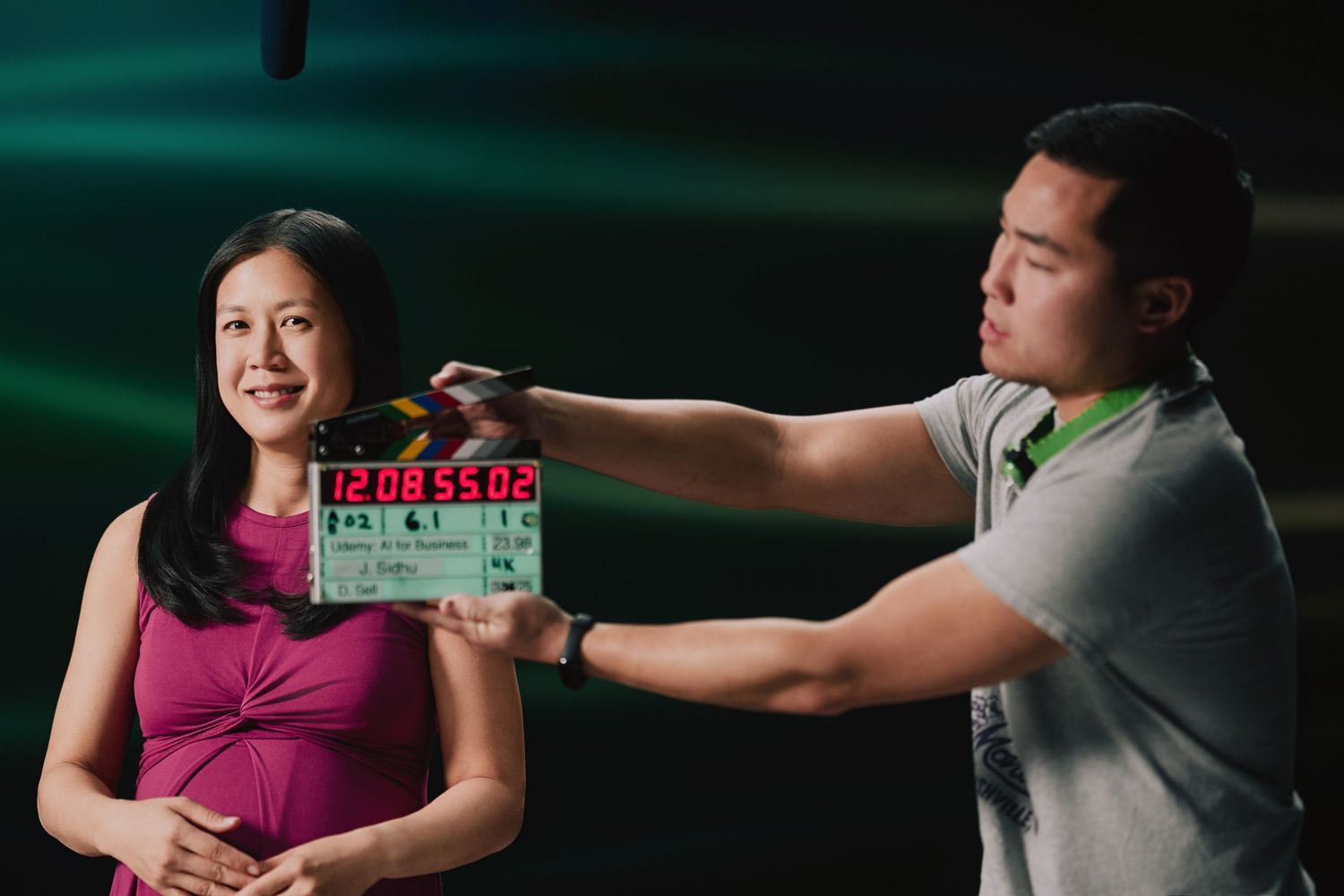 Behind-the-scenes film production shot with clapperboard being held in front of camera against green backdrop.