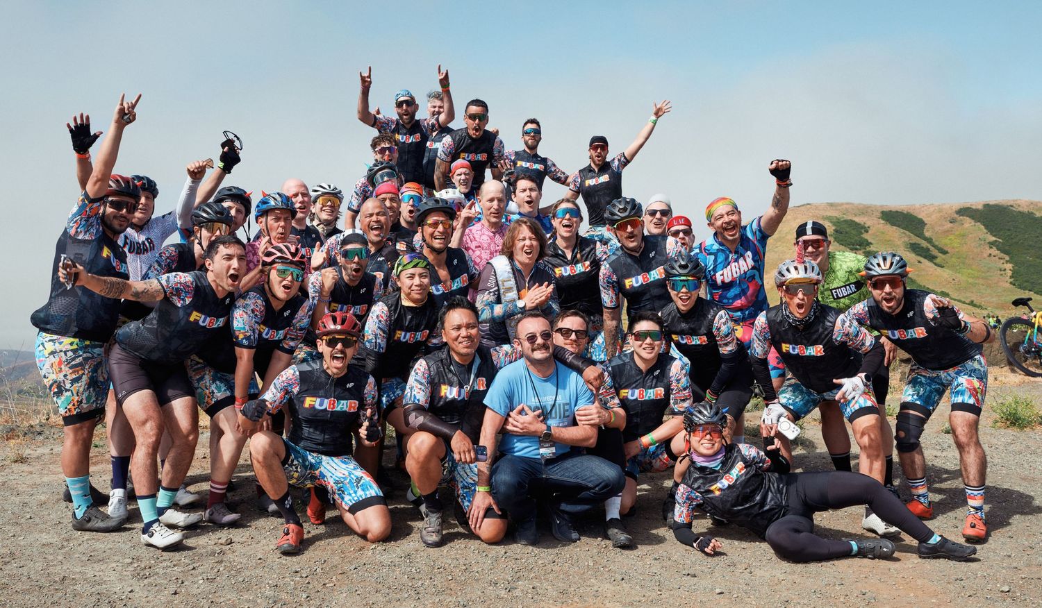 Large group of cyclists pose together for celebratory group photo on hilltop overlook.