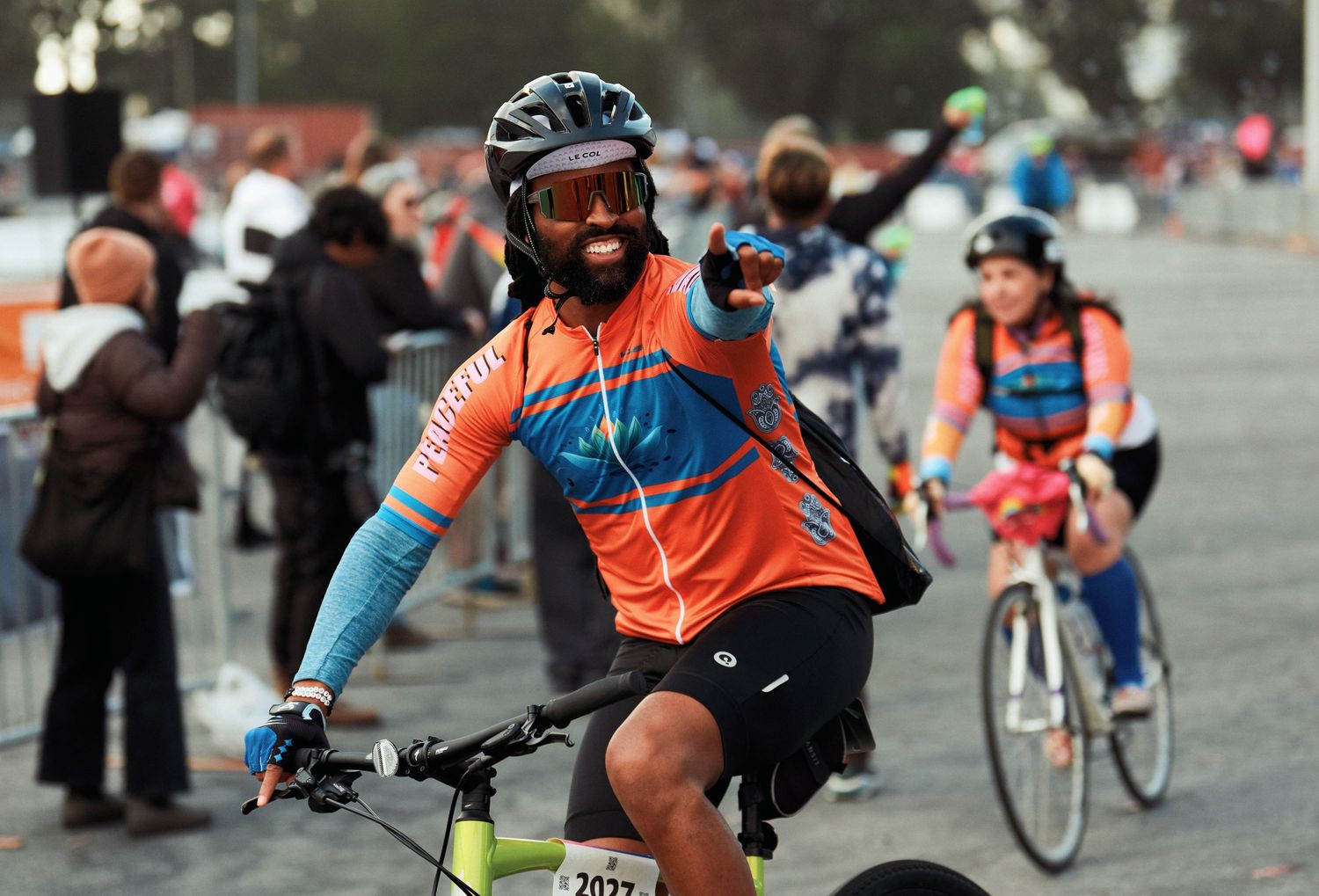 Cyclists ride in a group formation during a bike race, wearing bright orange and blue jerseys.