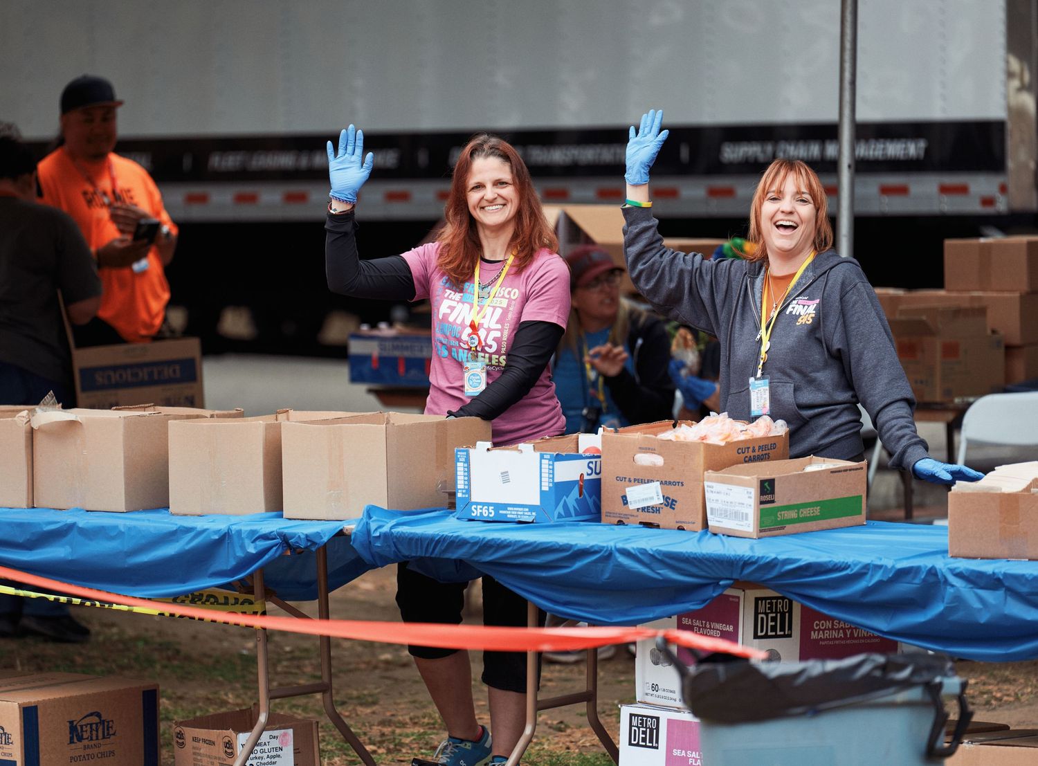 Volunteers in protective gloves working at a donation distribution table with boxes and supplies arranged on blue tarps.