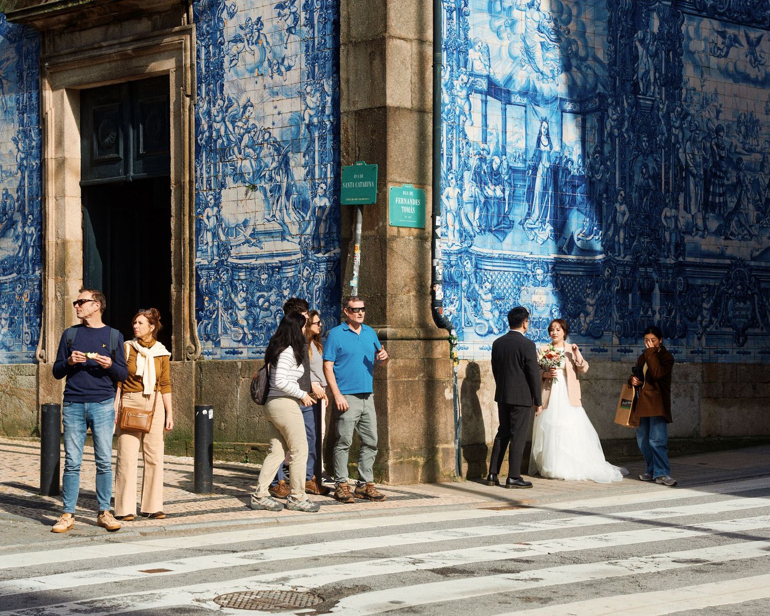 People gather outside a historic building with blue azulejo tiles in Porto, Portugal.