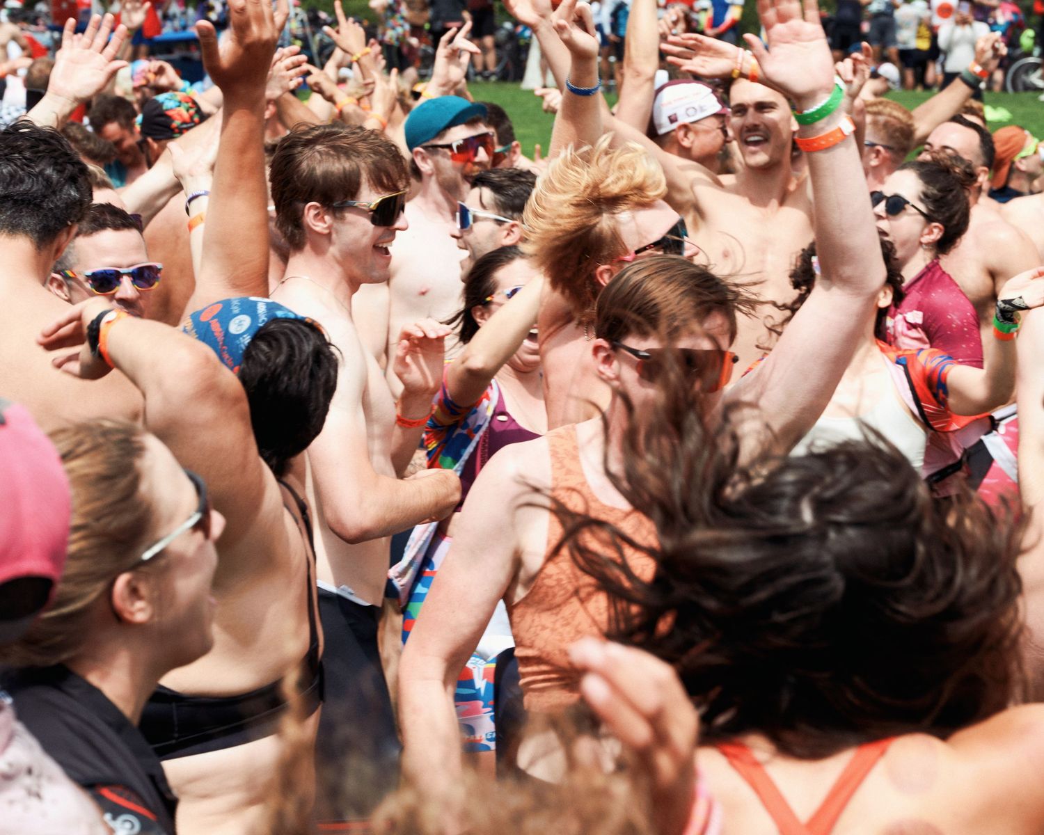 A large crowd of energetic people with raised arms dancing and celebrating at an outdoor festival event.