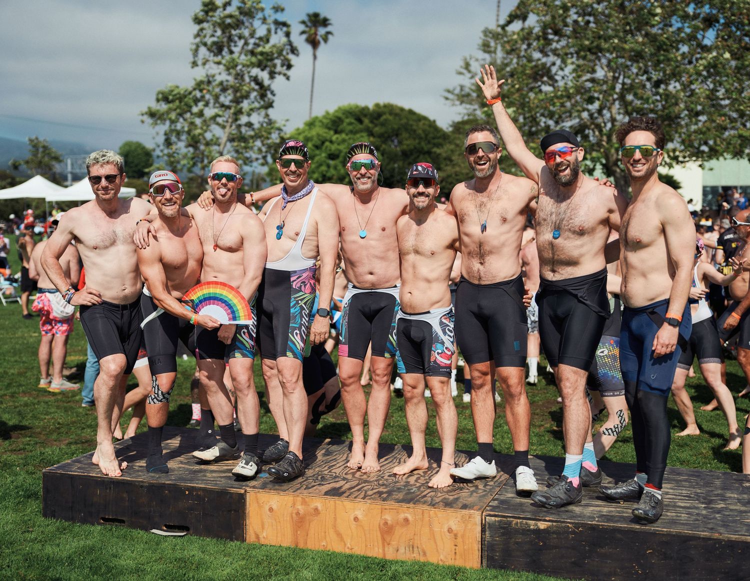 Shirtless participants gather outdoors for a casual social event on a sunny day with palm trees visible in the background.