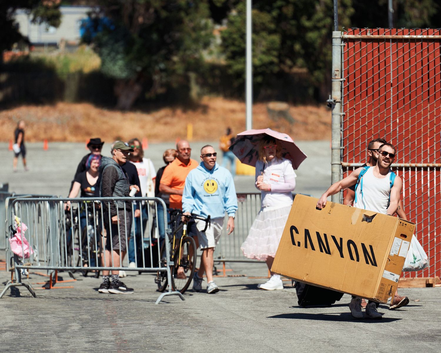 A person carries a cardboard CANYON sign while walking past spectators behind metal barriers at an outdoor event.