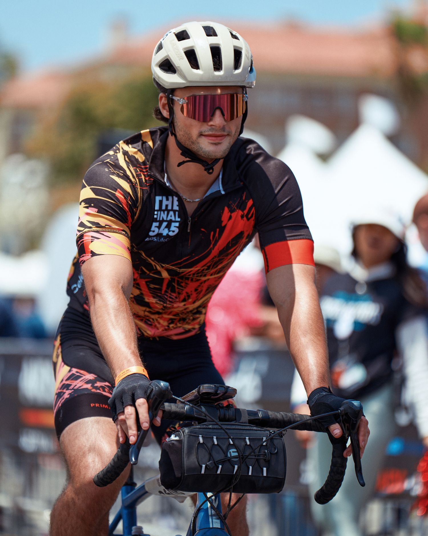 A cyclist wearing sunglasses and protective gear rides a bike during an outdoor event on a sunny day.