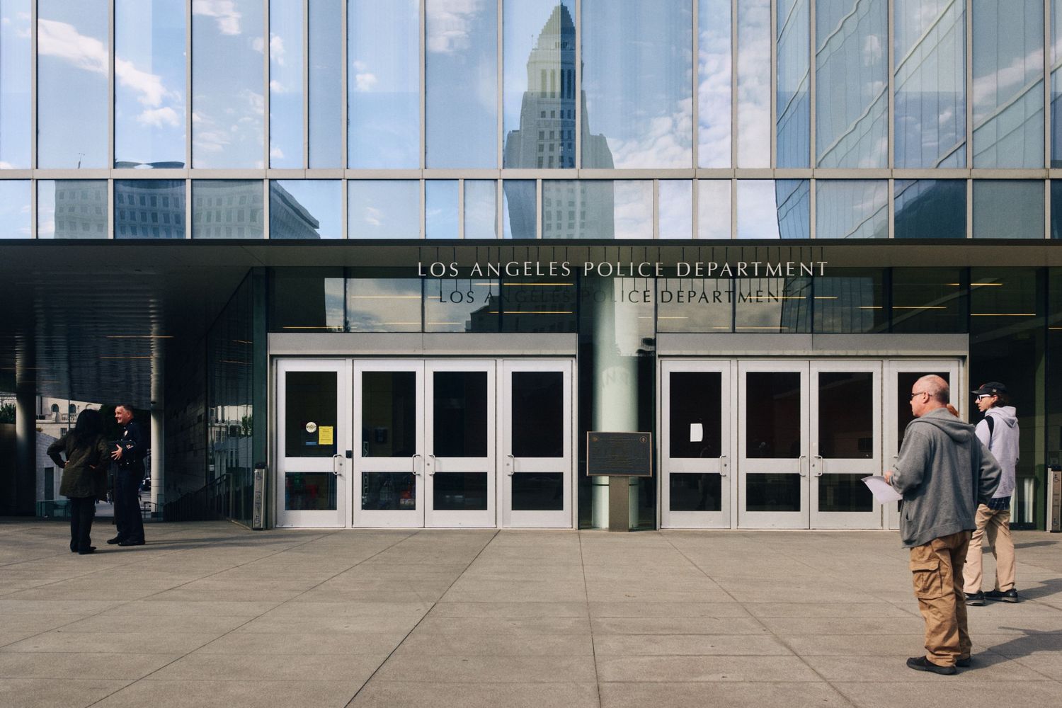 Los Angeles Police Department headquarters entrance with glass facade and pedestrians outside in downtown LA.