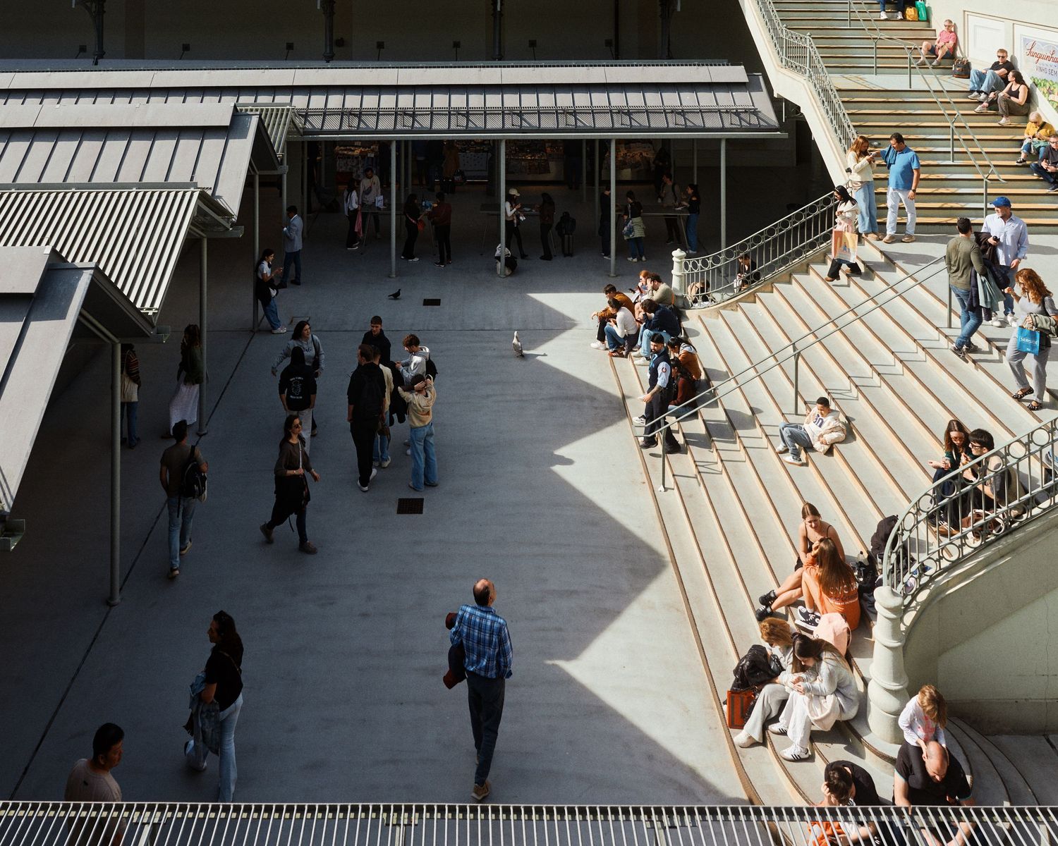 People gather on modern architectural steps and walkway with dramatic shadows at an urban public space.