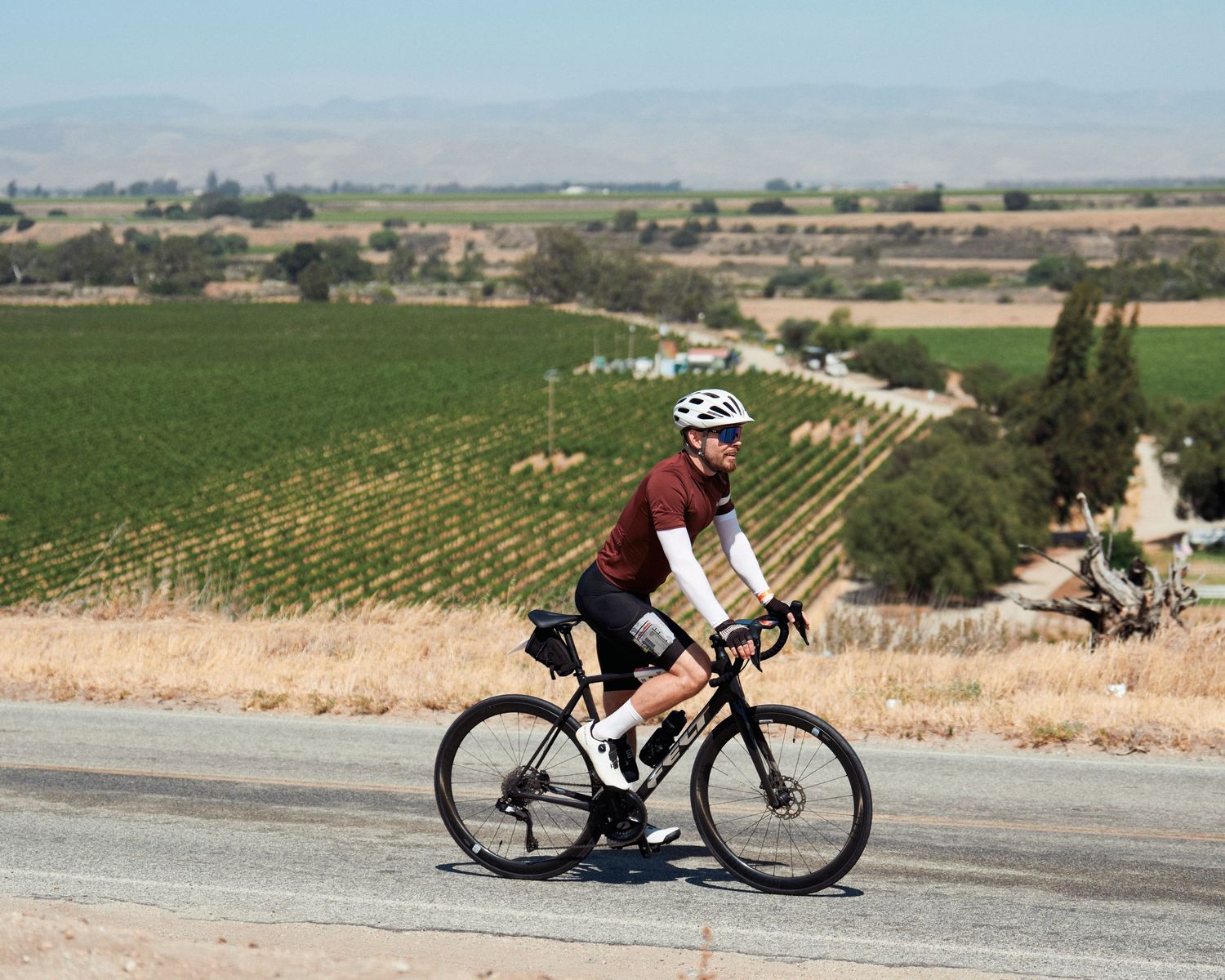 Cyclists riding road bikes through scenic rural countryside with mountains in background.