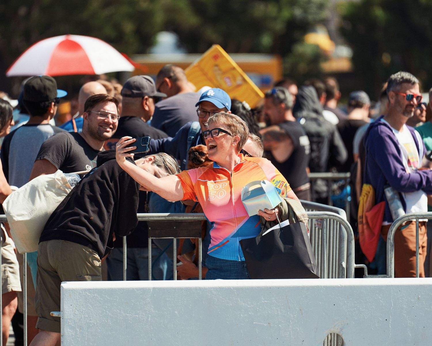 A person in an orange shirt and cap leans over a barricade within a crowded public event.