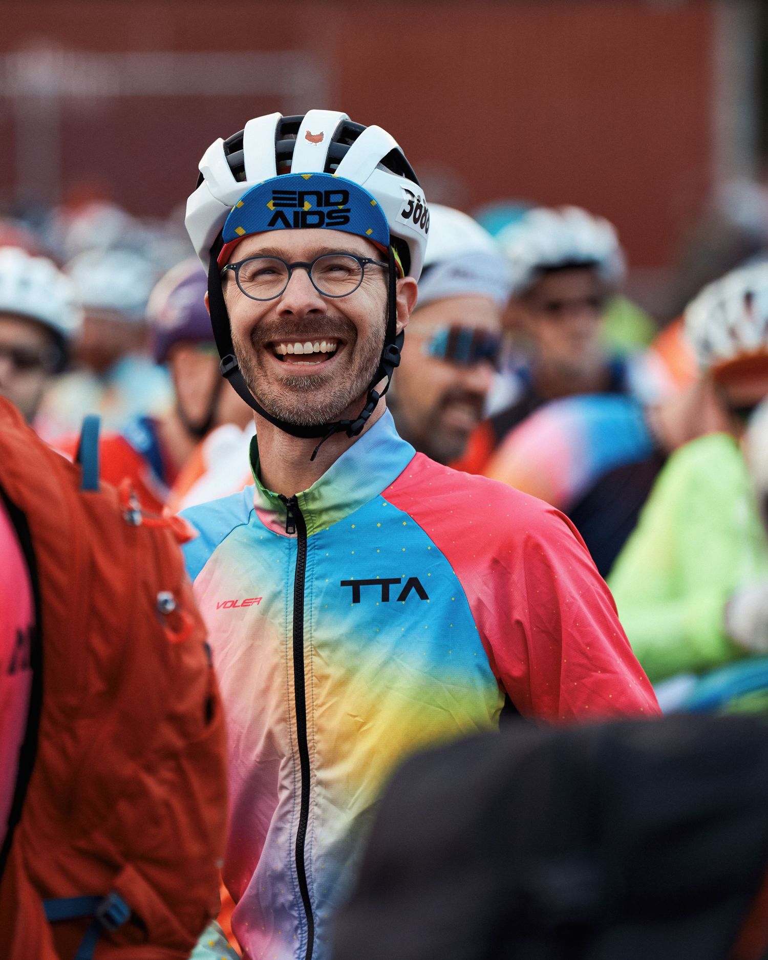 Cyclists in colorful jerseys and helmets participating in a group cycling event in cloudy weather.