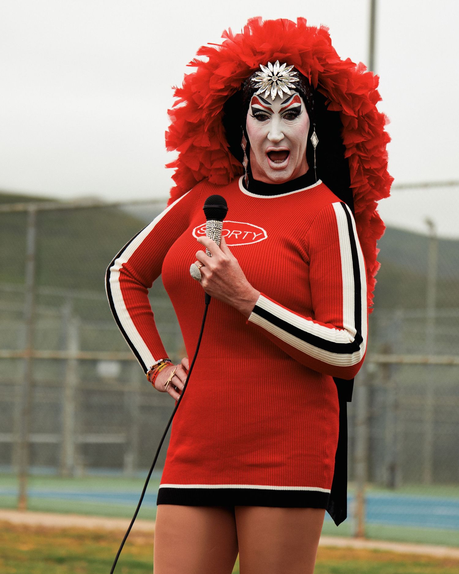 Person in a vibrant red outfit with matching puffy red headpiece poses energetically on a sports field.