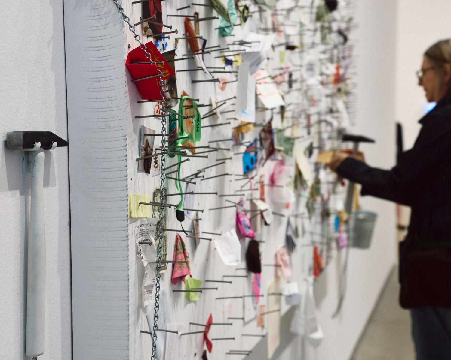 A visitor hammers a nail into Yoko Ono’s Painting to Hammer a Nail, a board already covered with brass nail heads, at The Broad.