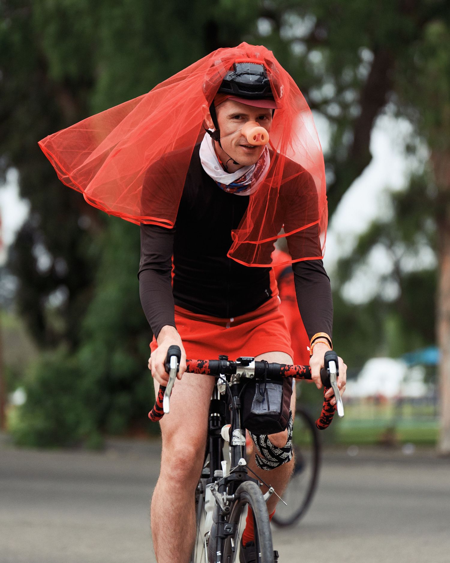 A cyclist wearing a flowing red veil rides a bike during a festive event.