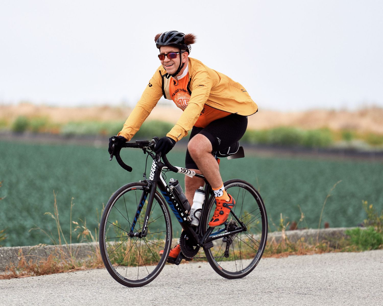 Cyclist in yellow jersey riding road bike along rural pathway with green fields in background.