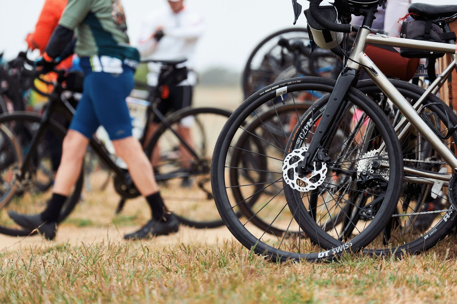 Close-up of bicycle disc brake and wheel with cyclists gathered in background.