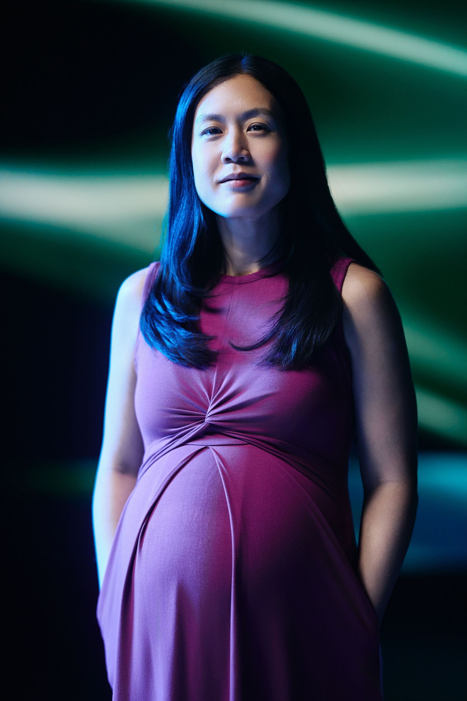 A person wearing a stylish pink sleeveless dress poses against a dark background with green lighting effects.