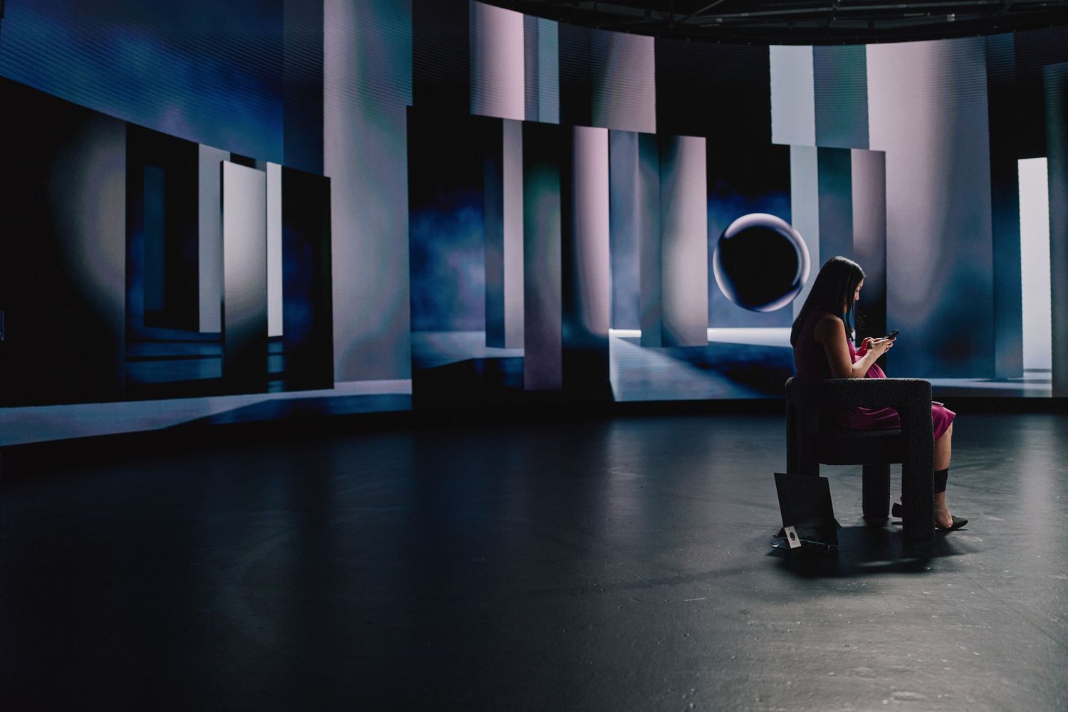 Figure sits in dim studio space surrounded by geometric lighting panels and modern architectural elements.