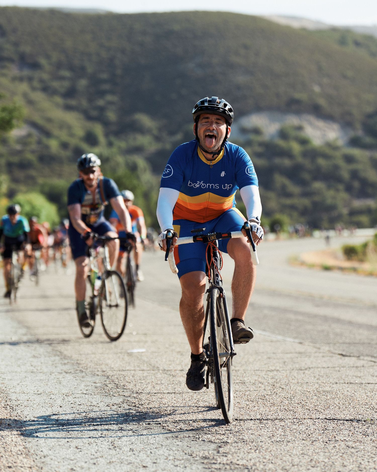 Cyclist wearing blue jersey riding road bike along coastal road during group cycling event.