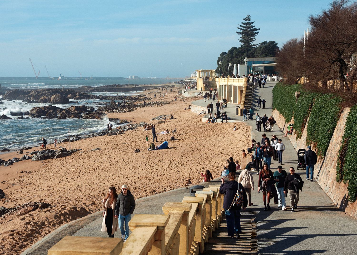 People walking along a coastal path with ocean views and sandy beaches on a sunny day.
