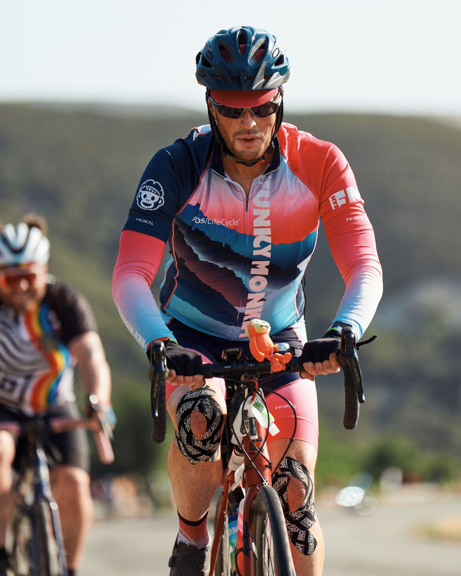 Cyclist in colorful blue and coral jersey riding road bike during outdoor cycling event on scenic mountain road.