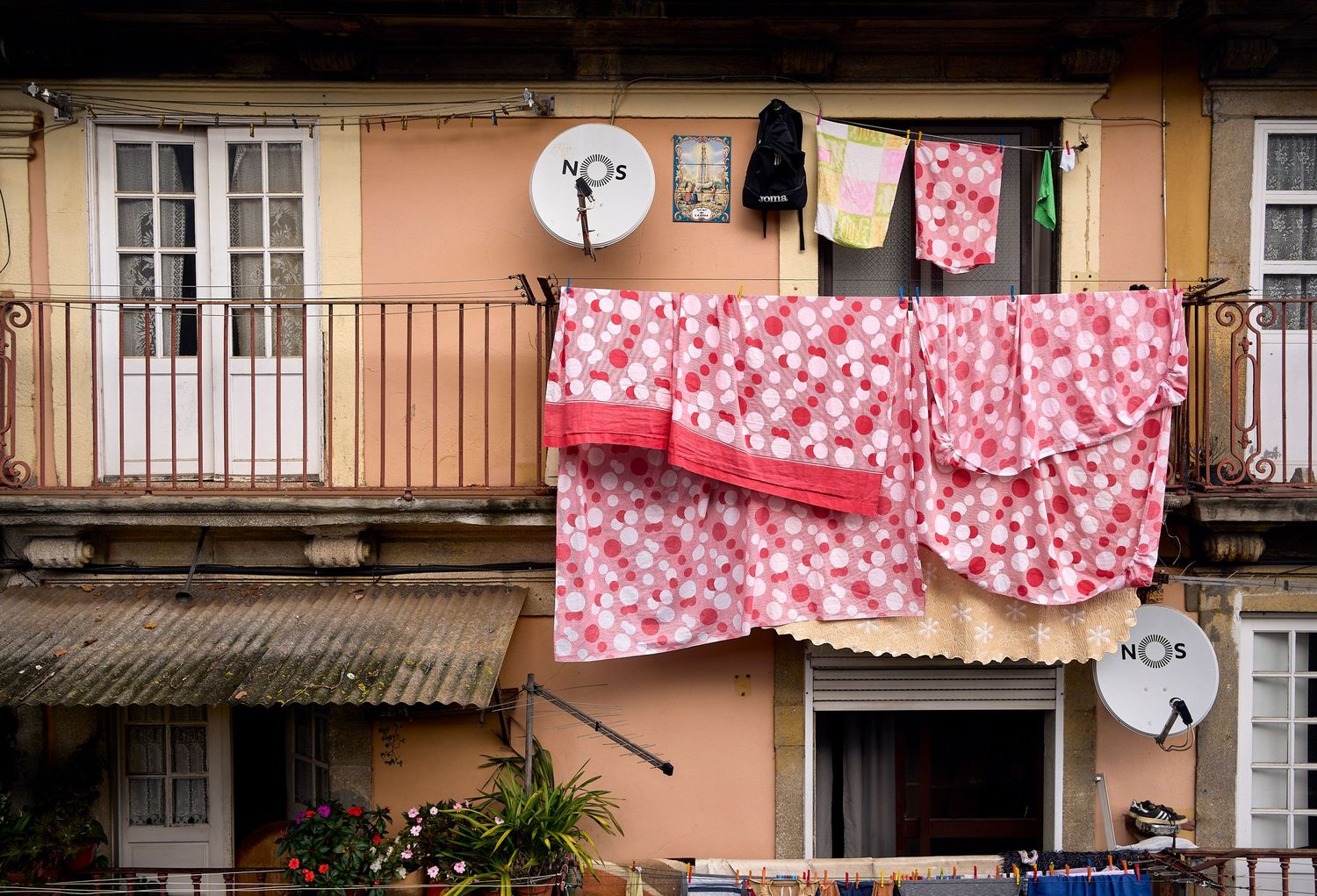 Pink and white floral bedsheets hanging to dry on clotheslines between residential buildings in an urban setting.