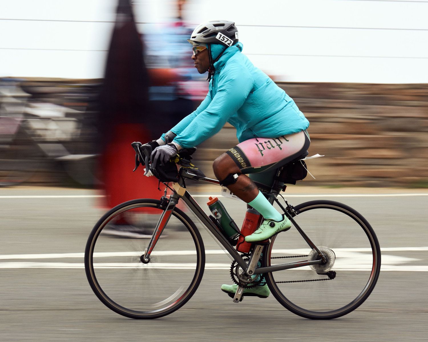 Cyclist in teal jacket rides red racing bike along road with motion blur effect.
