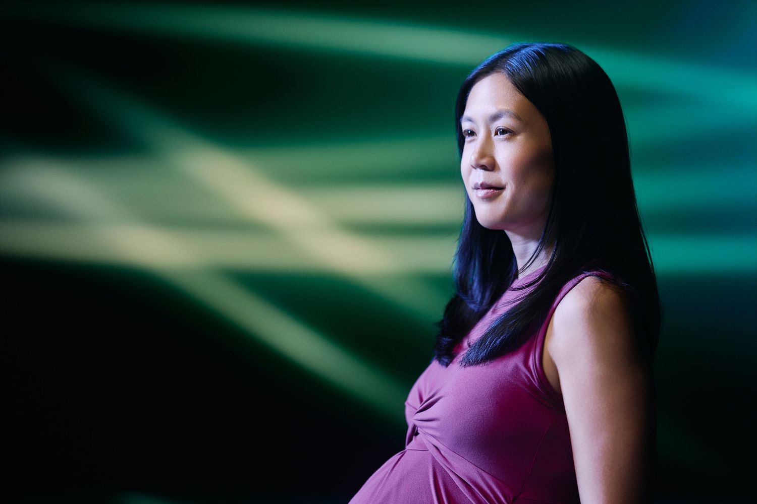 A person in a purple dress stands against a blurred teal and dark background with dramatic lighting effects.