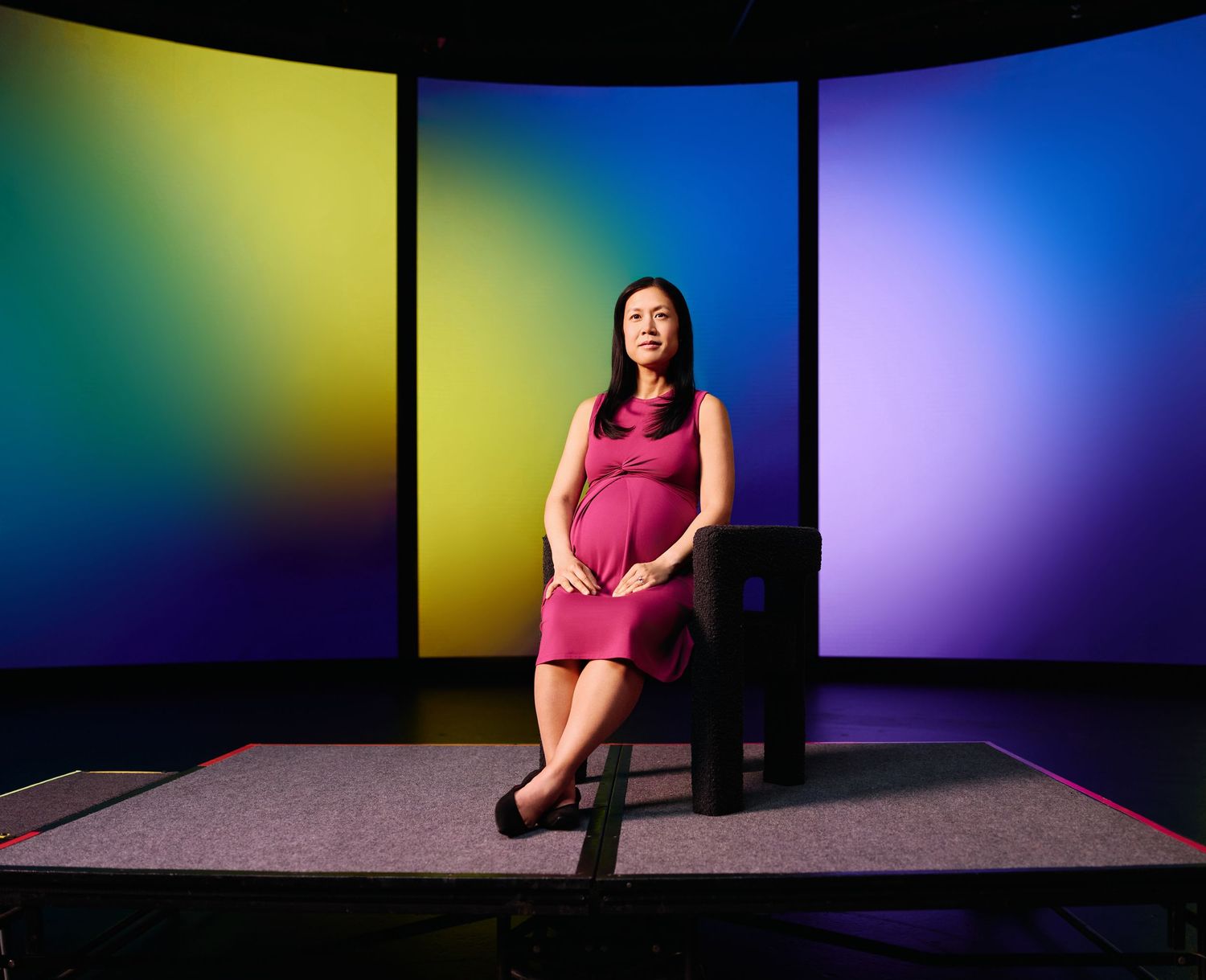 A pink-dressed figure sits in front of a vibrant backdrop featuring yellow, blue, and purple gradient colored panels.