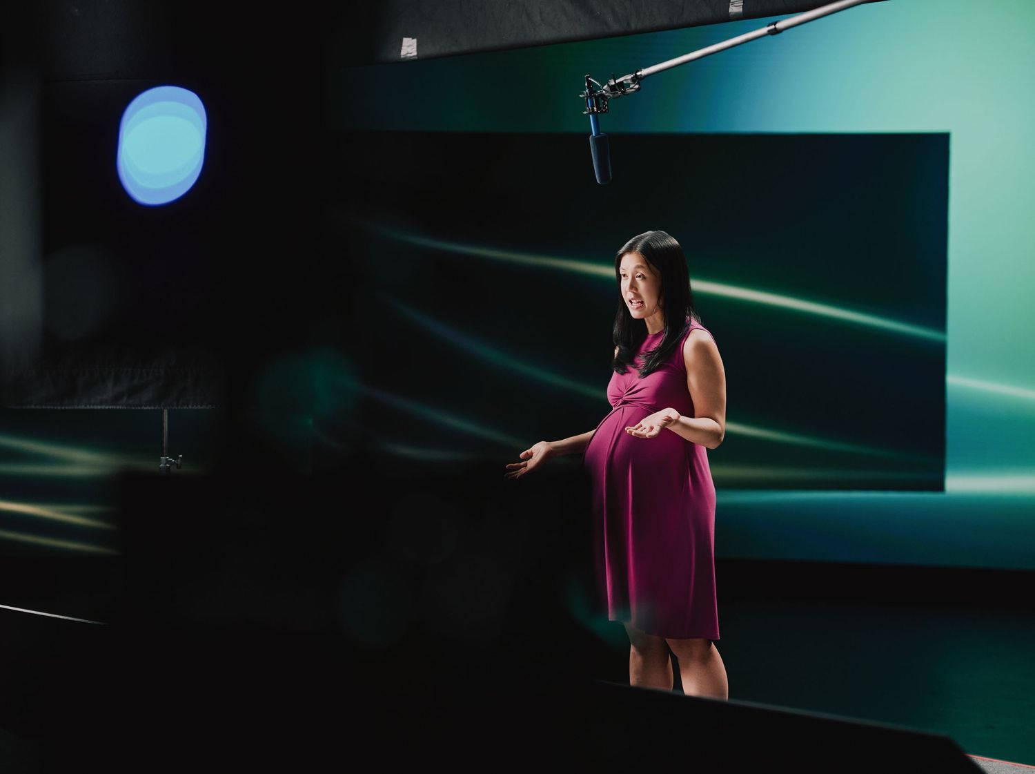 A performer in a magenta dress stands on stage with dynamic lighting and a green screen backdrop.